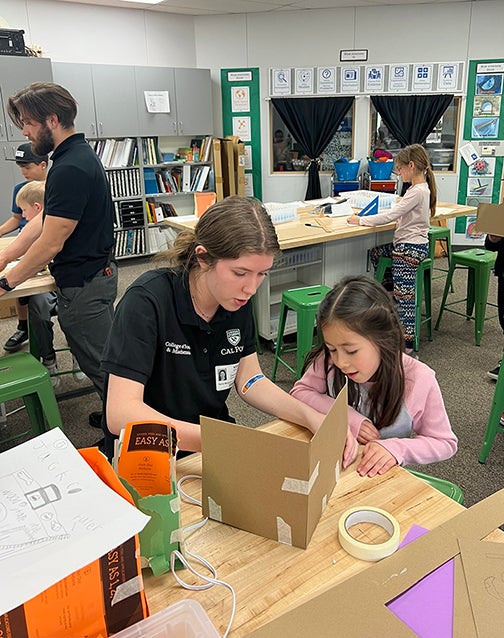 Two Cal Poly students are pictured assisting children with cardboard toolbox projects in an after-school Maker's Club at Santa Margarita Elementary School.