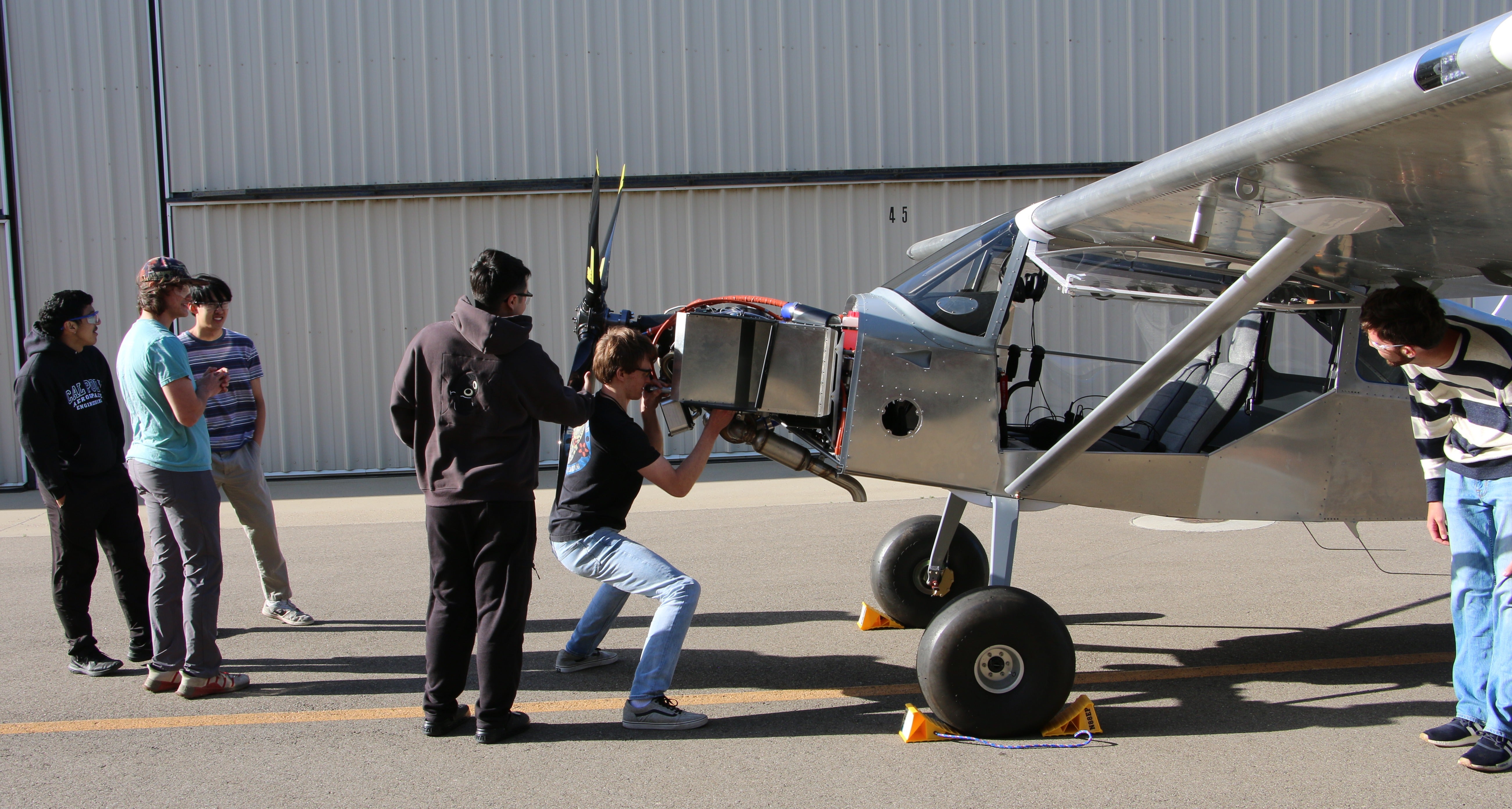 Students perform final checks on a metal aircraft before its first startup at the airplane hangar.