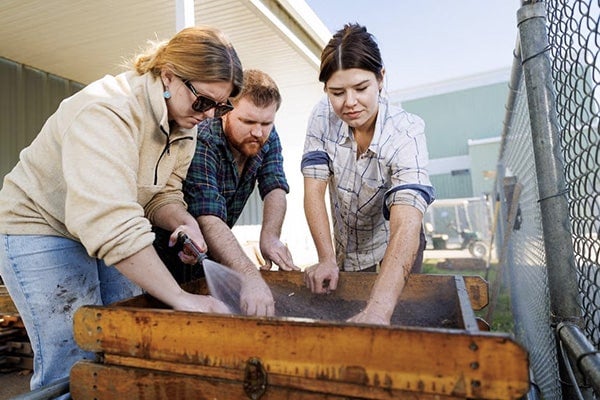 Three students analyze artifacts on a wet screen frame.