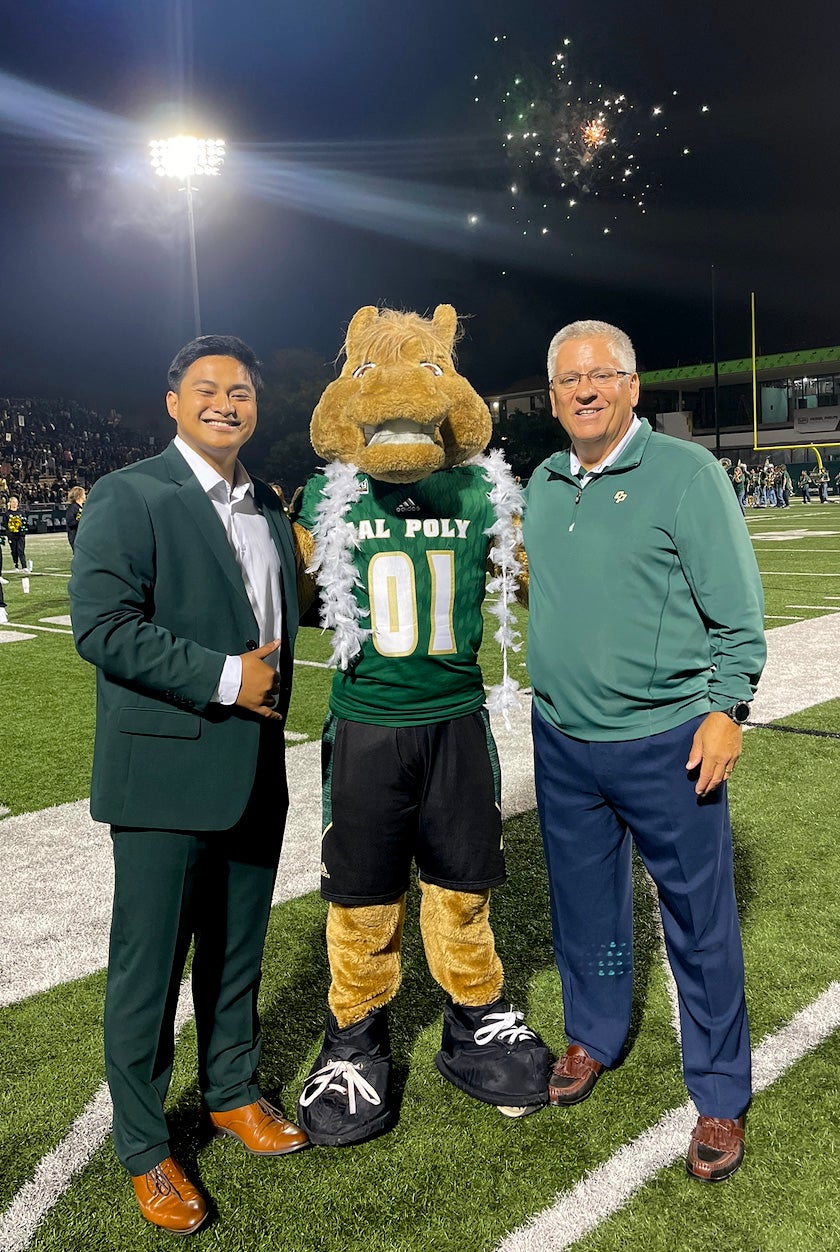 Marc Cabeliza poses with Jeffrey Armstrong and Musty the Mustang on the football field.