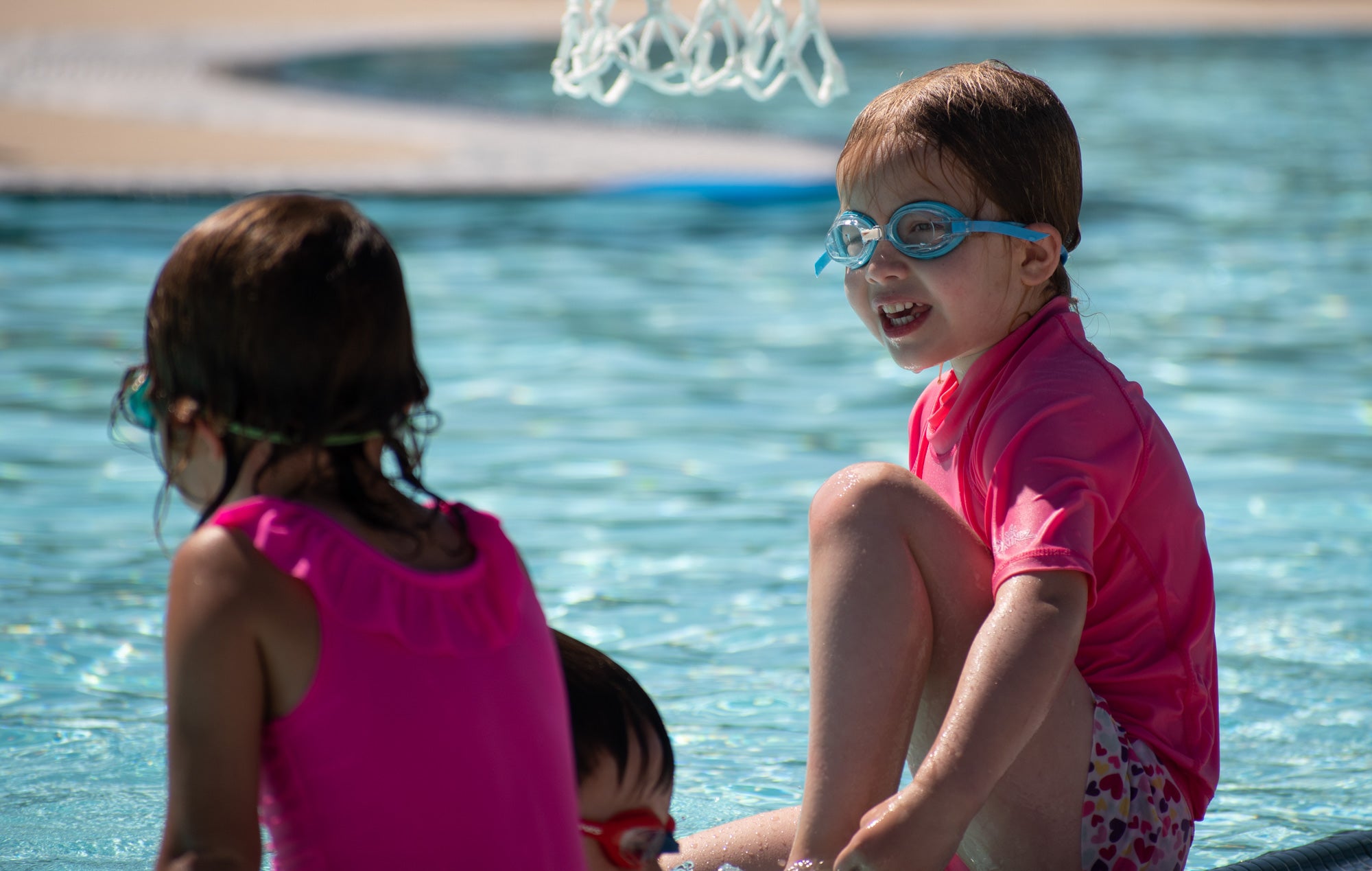 Two young children sit on the deck of a pool.