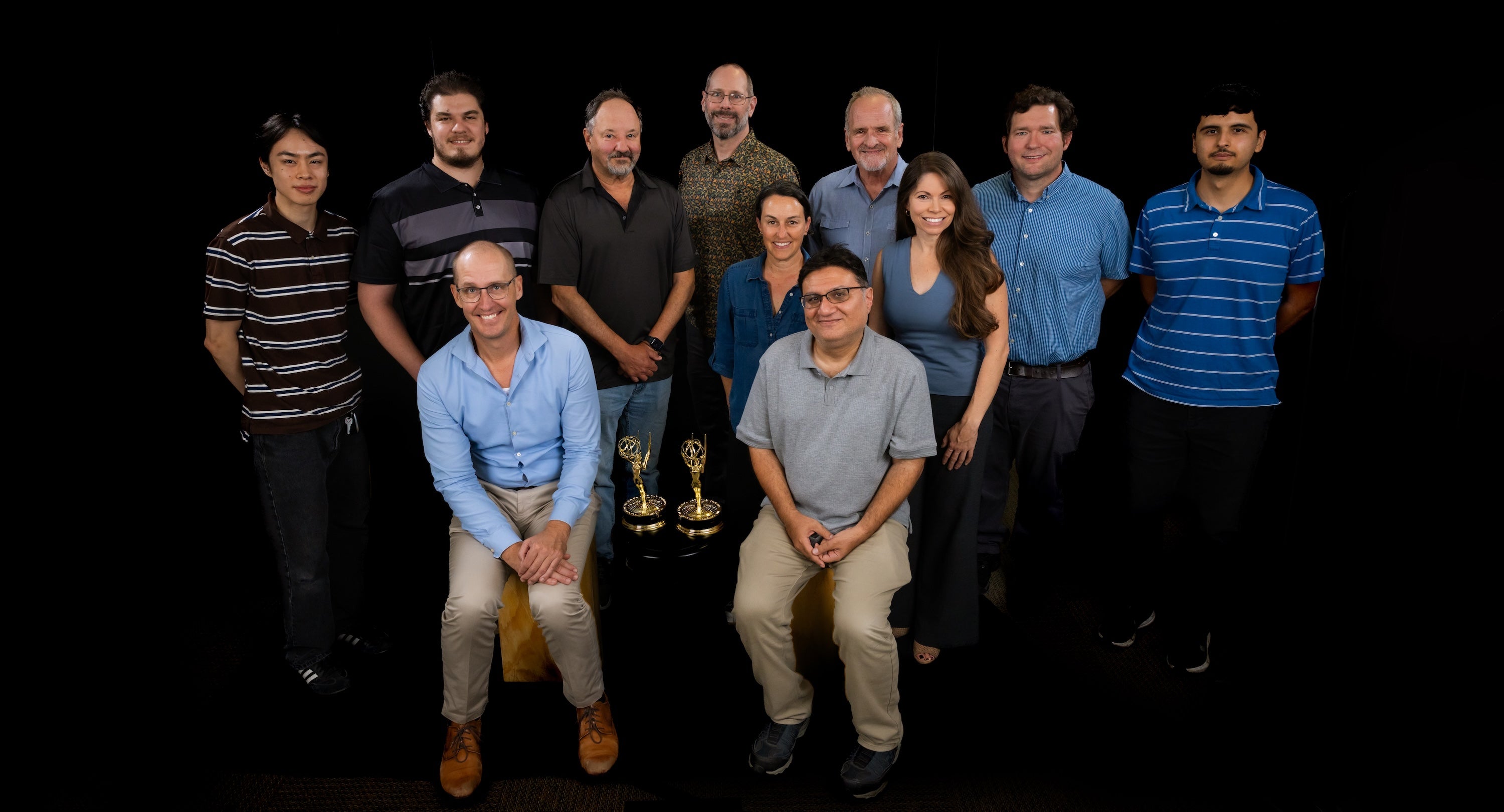 A team of CalMatters reporters and Cal Poly students and professors pose in front of a black background with two Emmy statuettes.