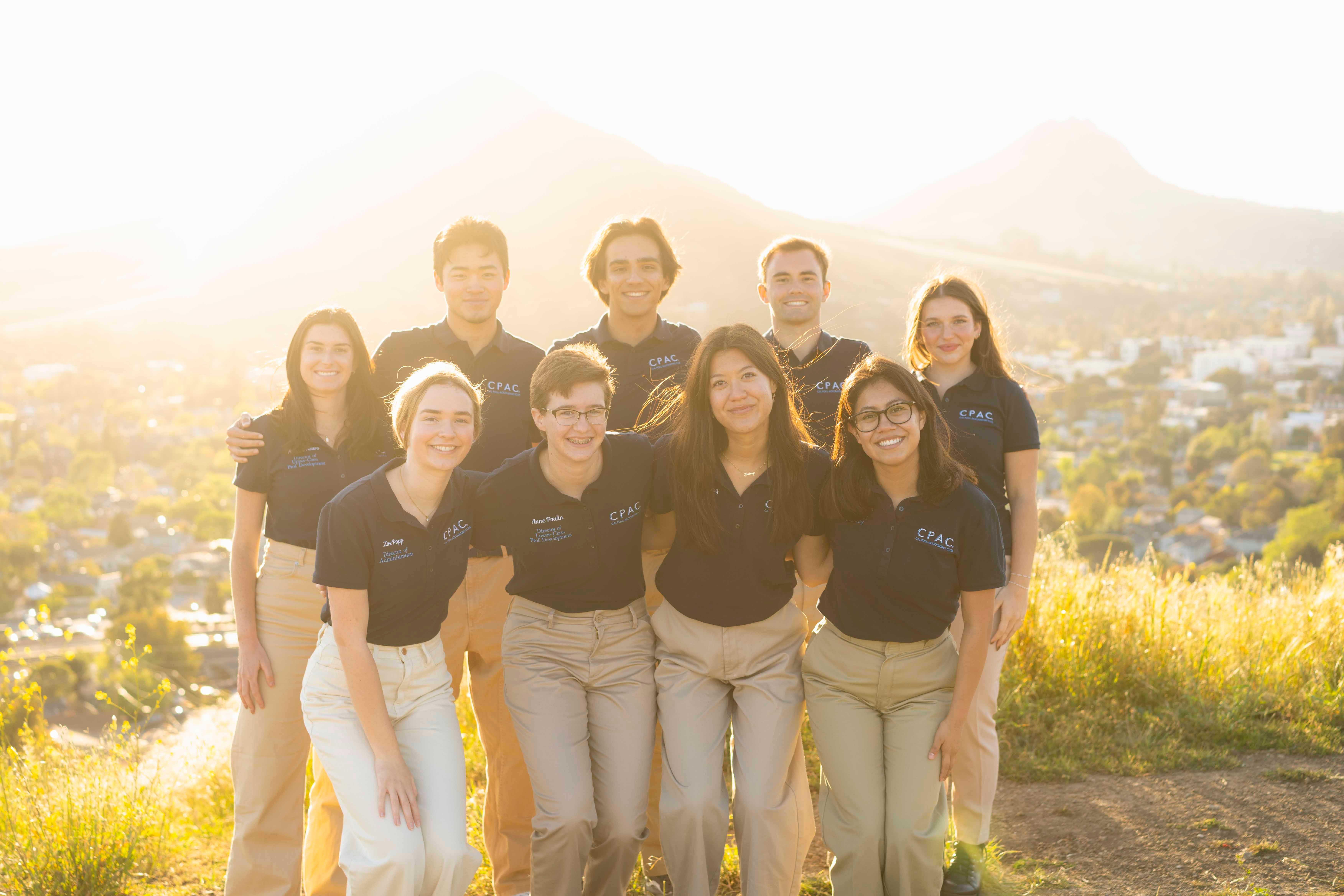 A group of students wearing polos smiles for a photo outside.