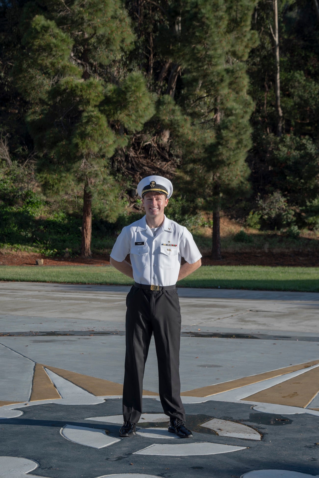 A student in a maritime uniform poses for a photo in front of pine trees.