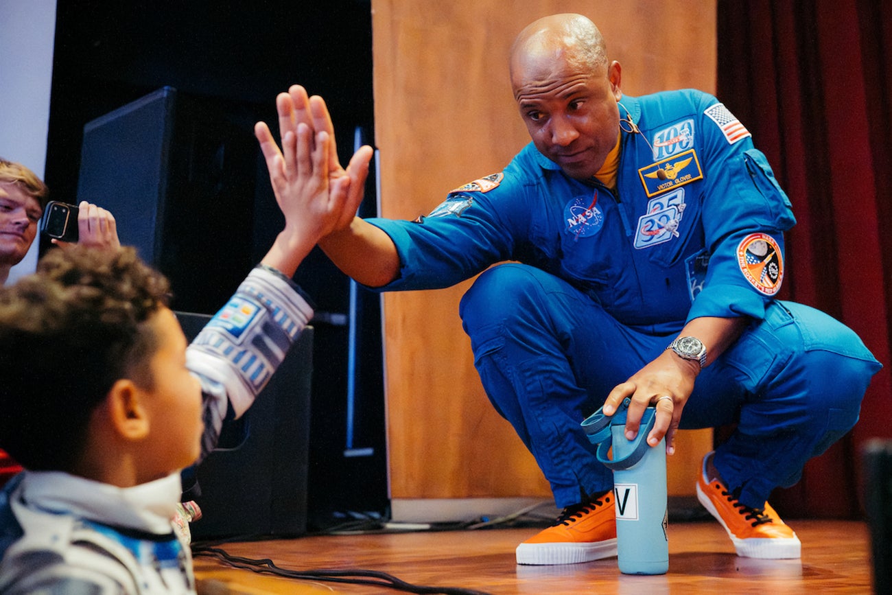 A man in a blue NASA jumpsuit gives a young boy a high five