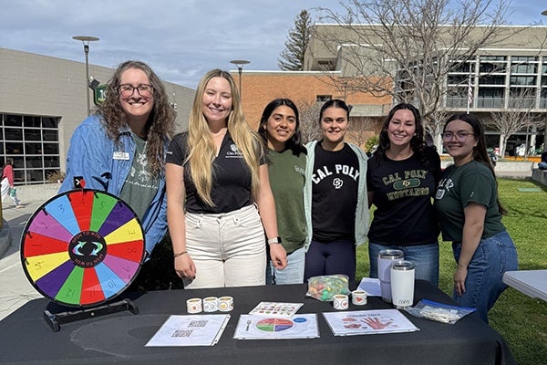 A group of students stand behind a table with information on health and wellbeing. 