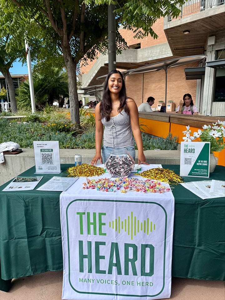 A student smiles at a green booth on campus.