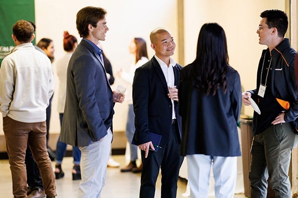 A group of people speak with each other while holding drinks at an event. 
