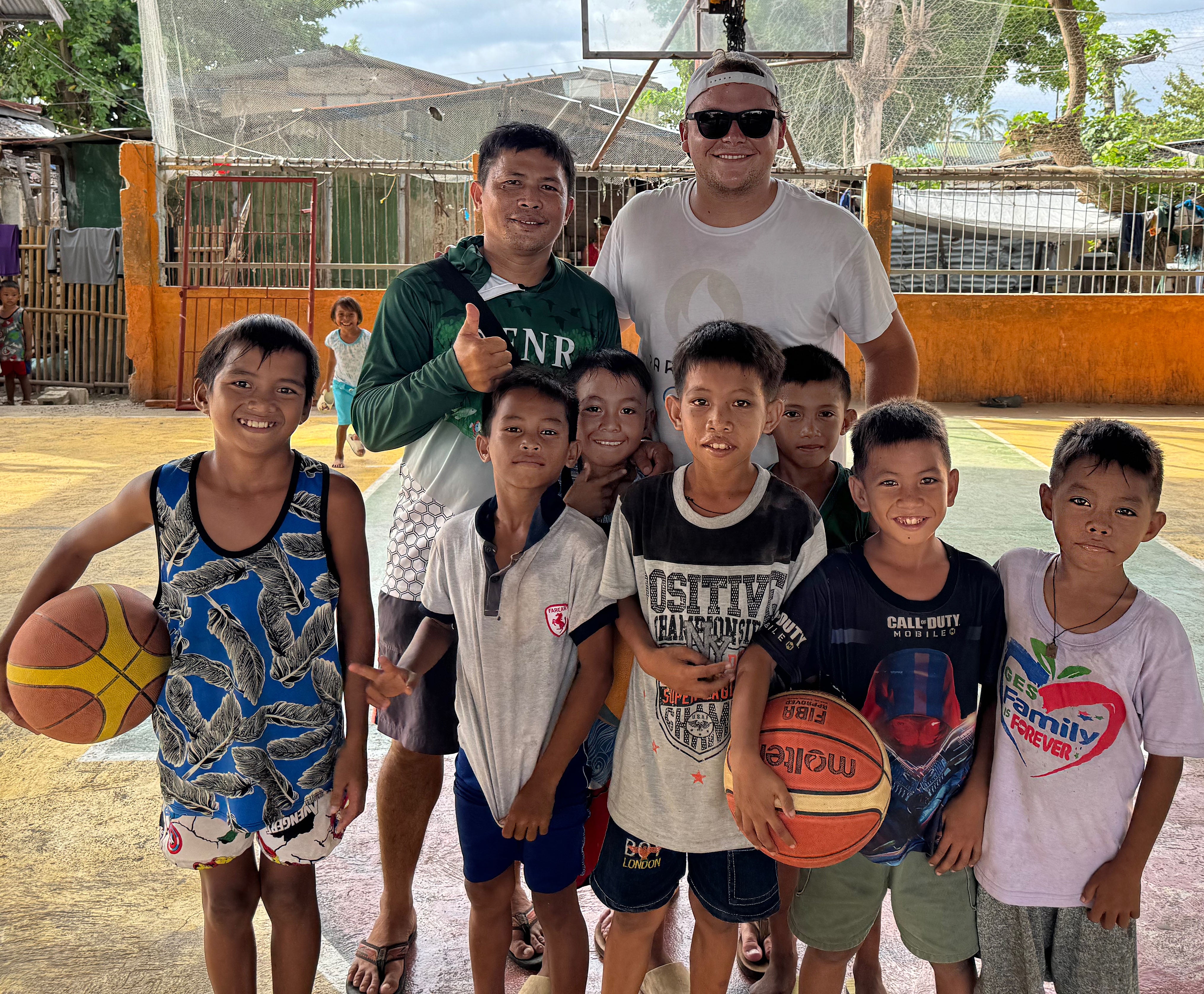 Julia, in the back, smiles with children on a basketball court.