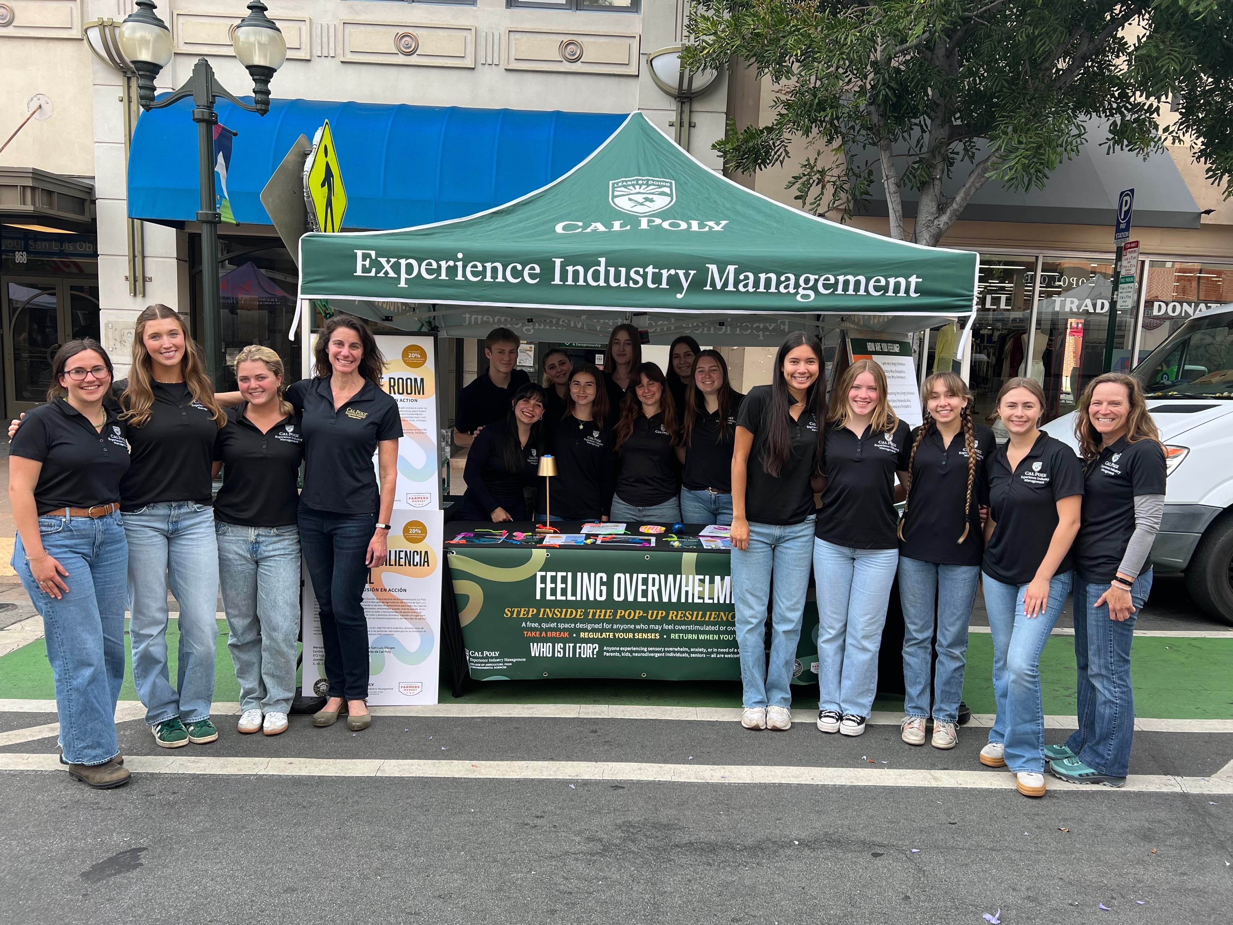 A group of experience industry management students pose with their booth at farmers market.