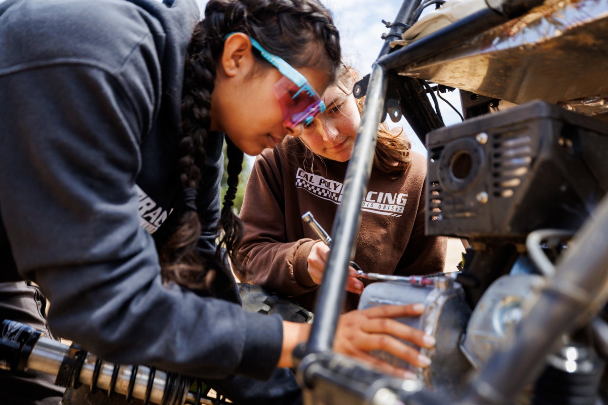 Two Cal Poly Racing team members in team sweatshirts use tools to repair the baja vehicle