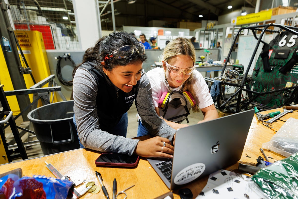 Two Cal Poly Racing team members work at a laptop in the aero hangar