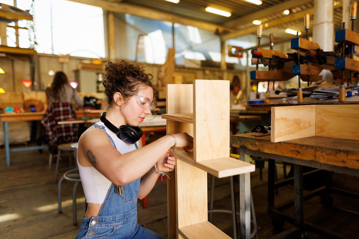 A student kneels next to a wooden frame in a fabrication shop