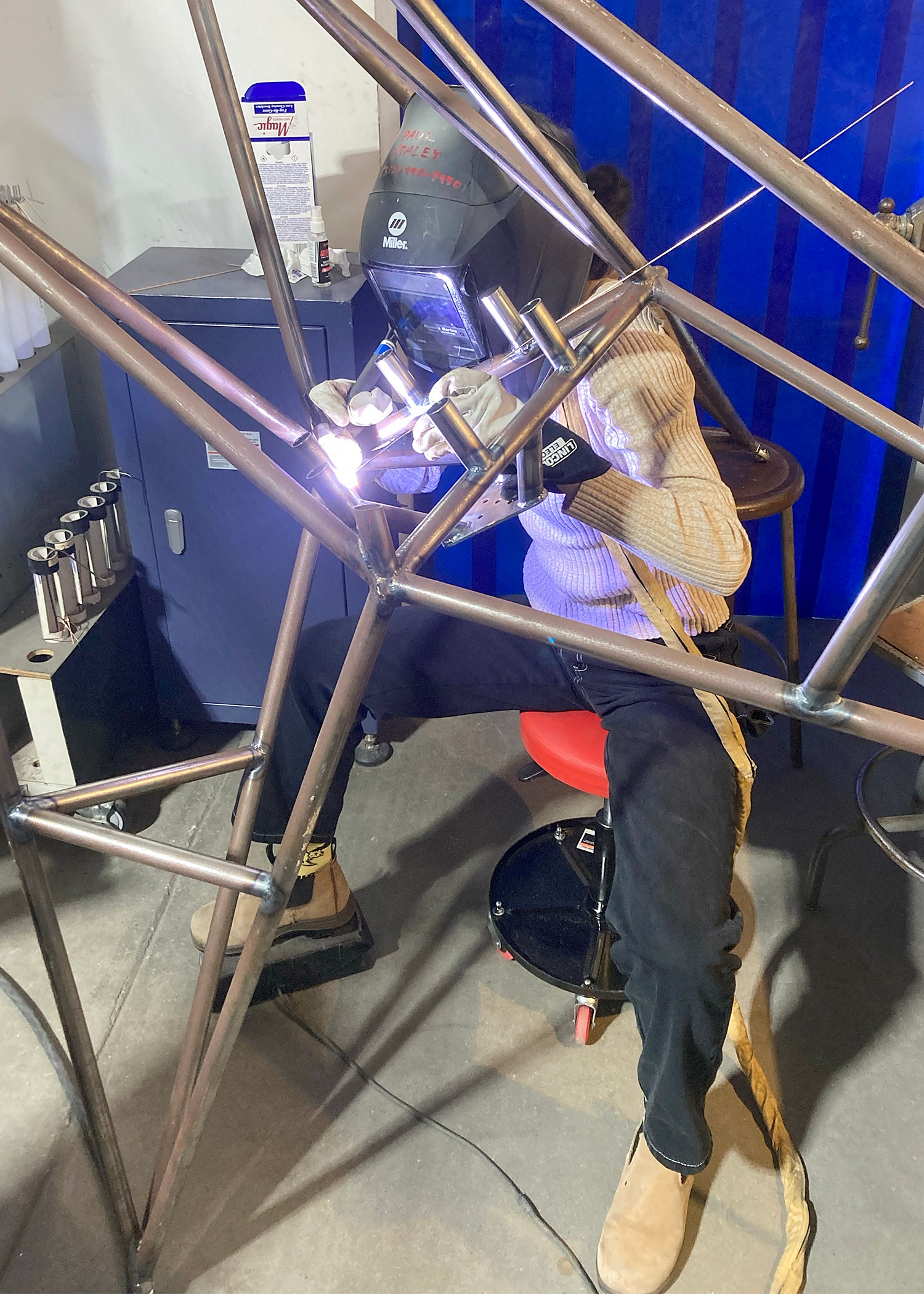 A student wearing a welding mask works on a rocket engine.