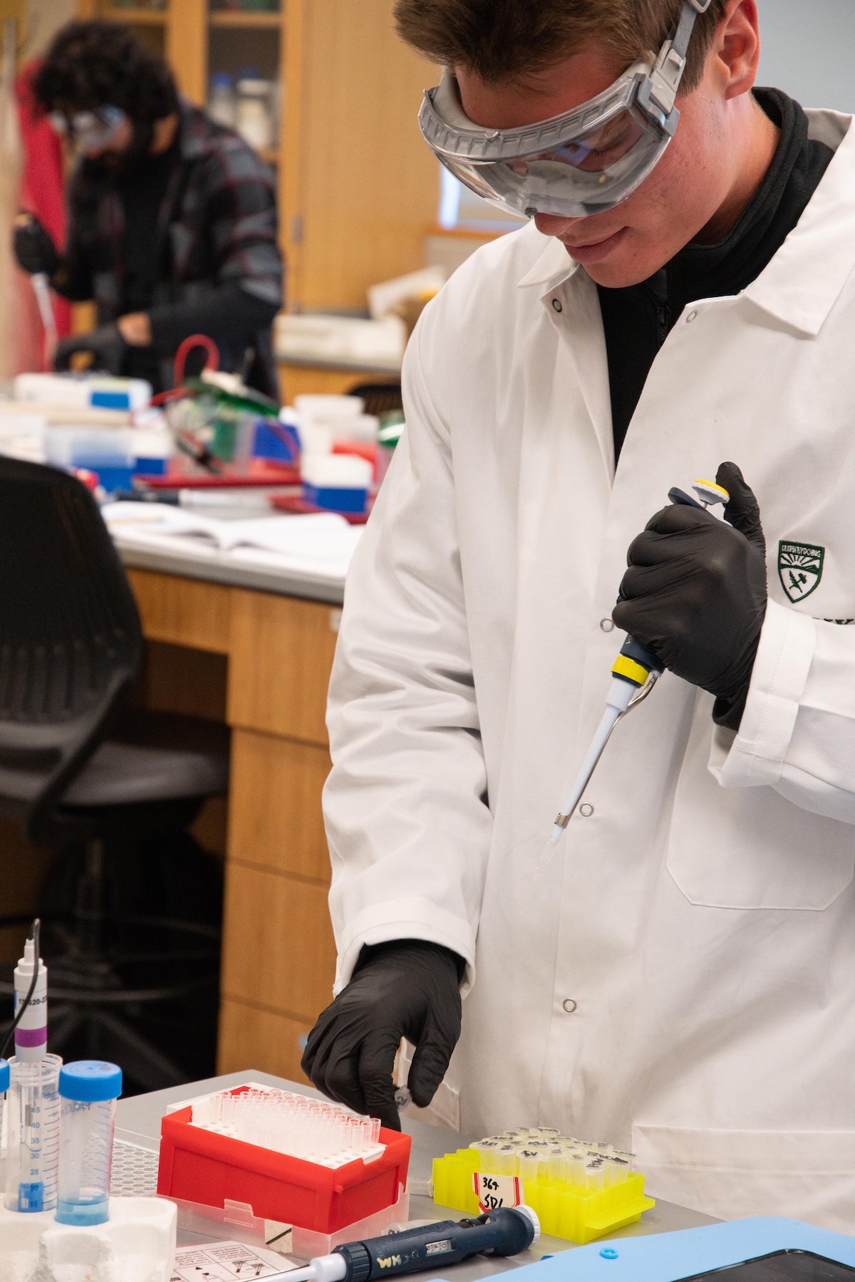 A student wearing lab gear uses a syringe.