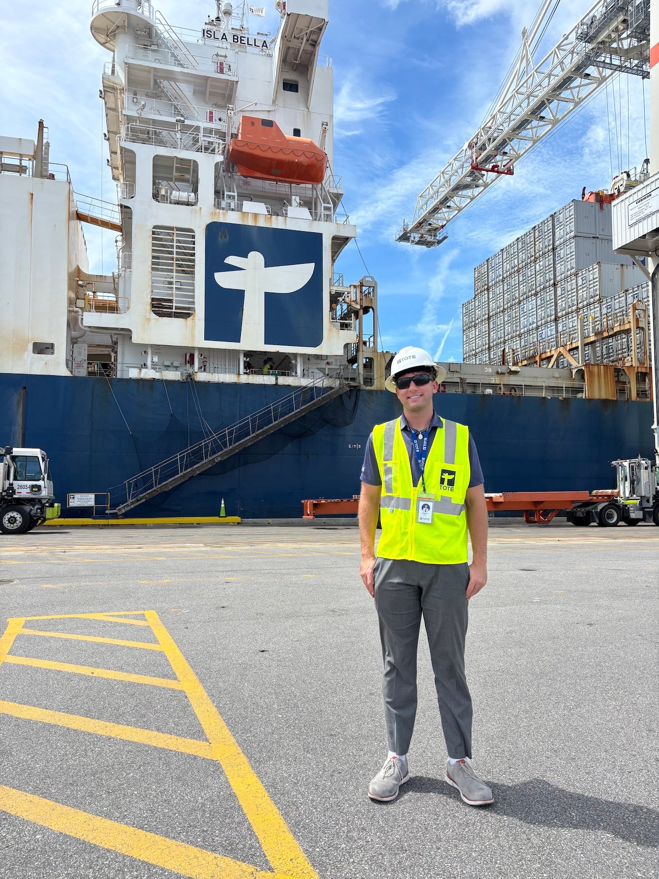 A student wearing a high-visibility vest stands in front of a ship.