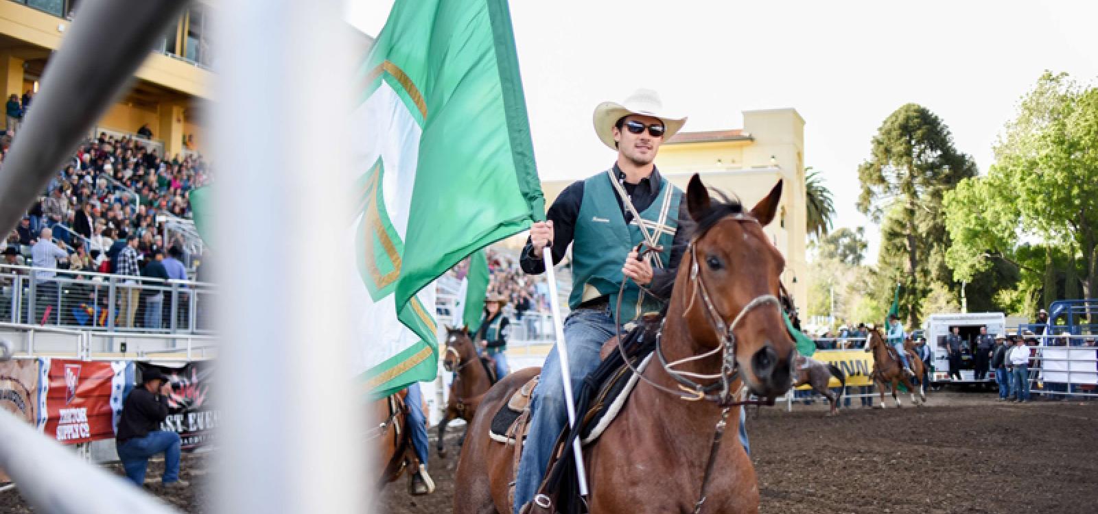 A student rides a horse and carries a flag at the Poly Royal Rodeo in 2017.