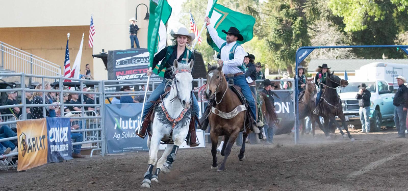 Students ride horses and carry flags around the arena at the 2019 Poly Royal Rodeo.