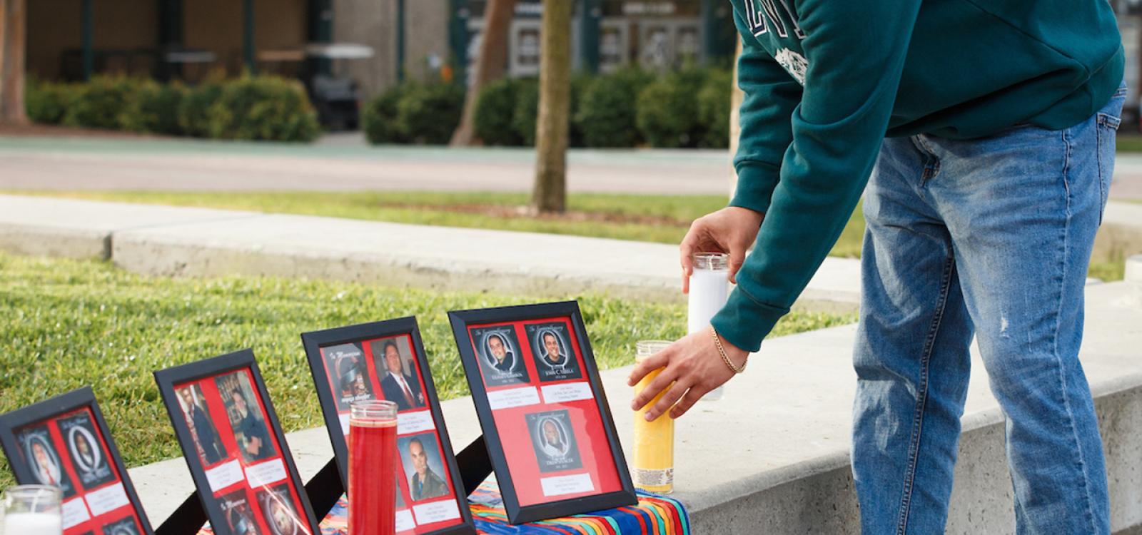 A young man places candles in front of framed photos at an outdoor ofrenda