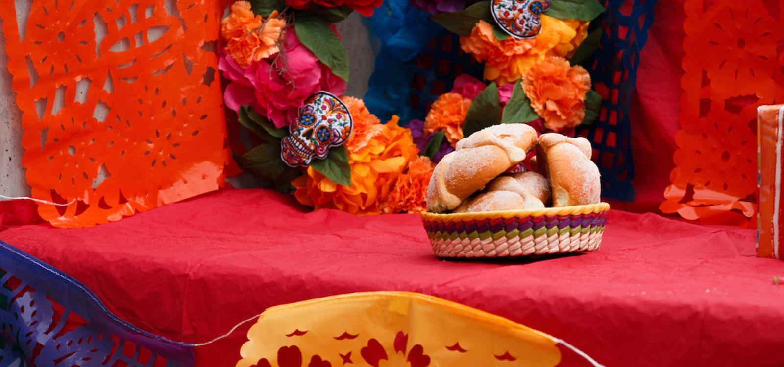 An ofrenda decorated with a flower wreath and a basket of pan de muerto.