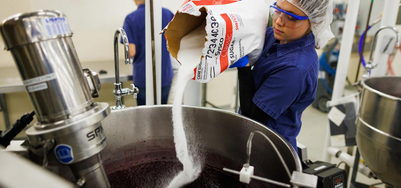 A student adds sugar to a vat of blackberry jam in the Cal Poly food pilot plant.