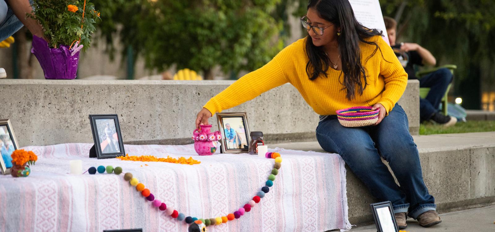 A student adjusts a small pink vase on an ofrenda.
