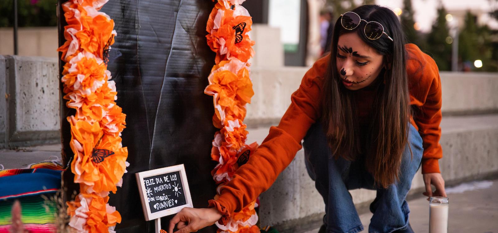 A student places a small orange paper butterfly on an ofrenda.