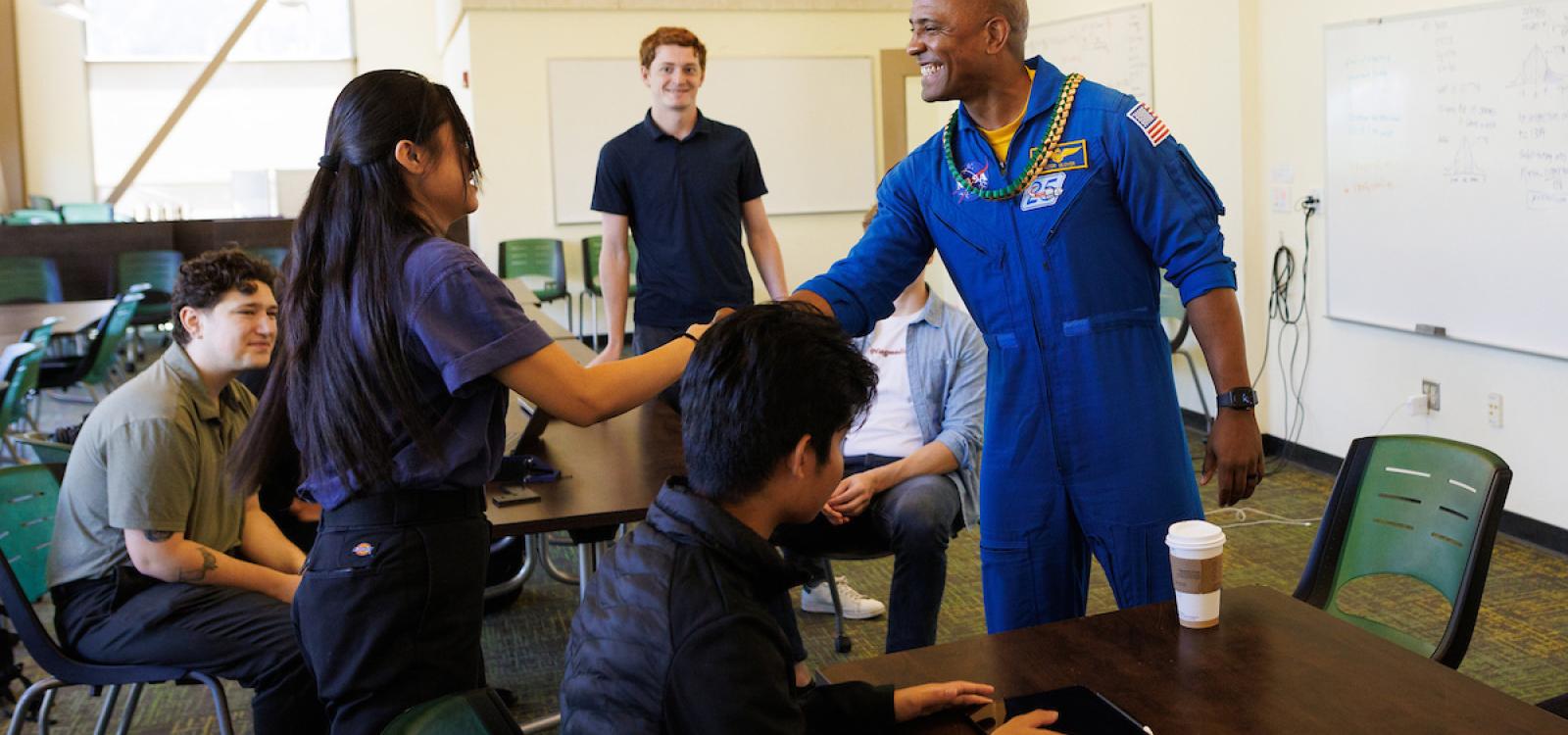 Victor Glover shakes hands with students working on constructing a model Mars rover after they presented him with a graduation lei.