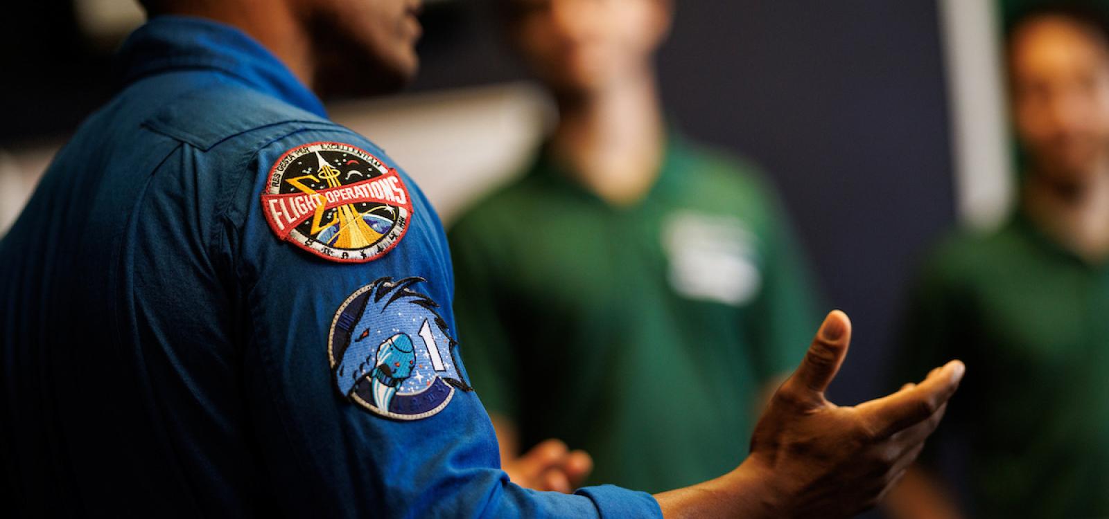 A closeup of the patches on Victor Glover's jumpsuit as he speaks to students.