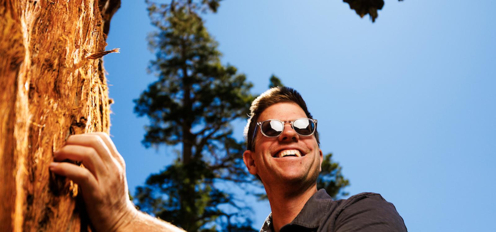 Matt Ritter smiles and poses with the Bennett Juniper during tree measuring.