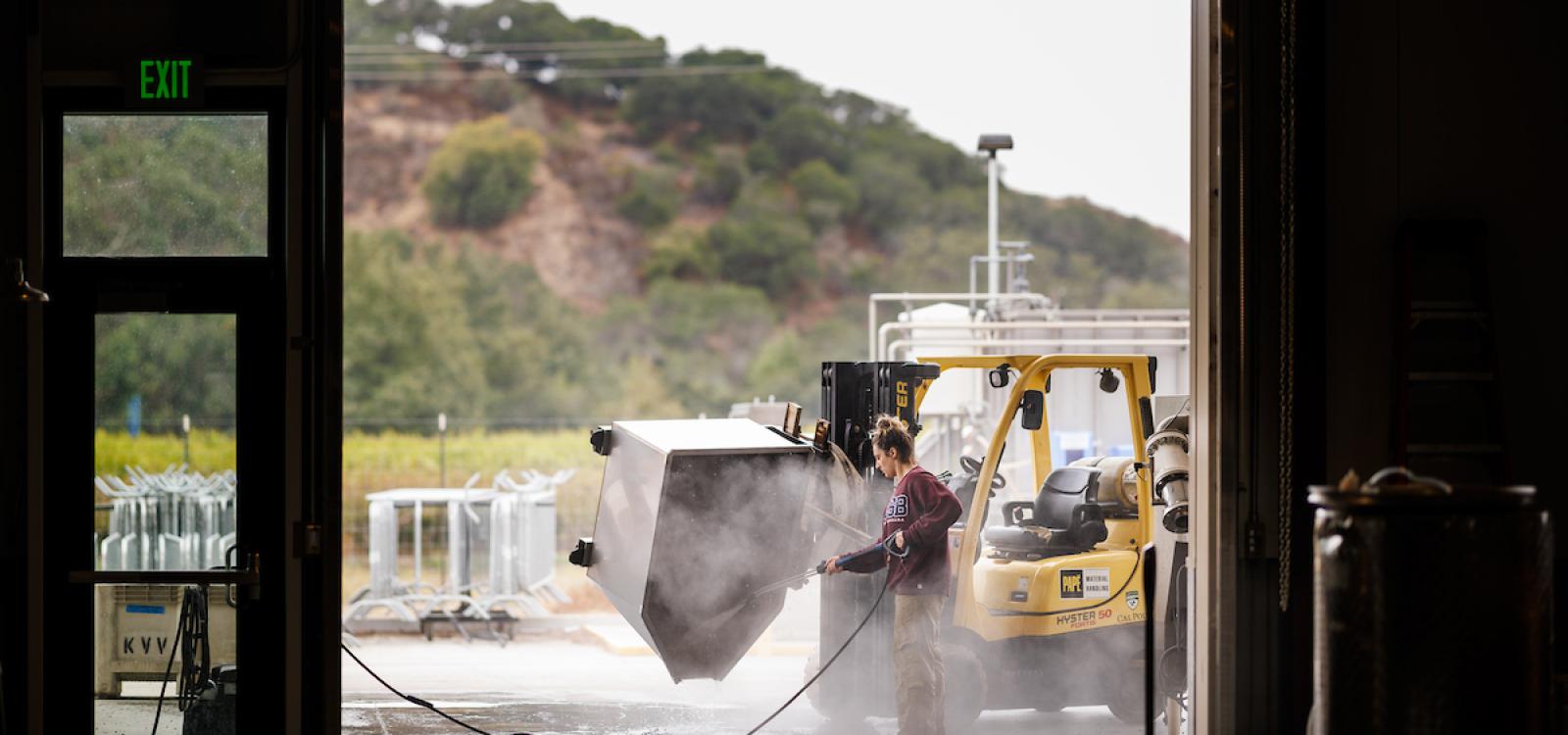 A student sprays down some machinery during grape processing.