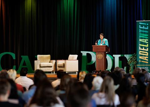 Dolores Huerta stands behind a podium at Chumash Auditorium with the audience visible in foreground