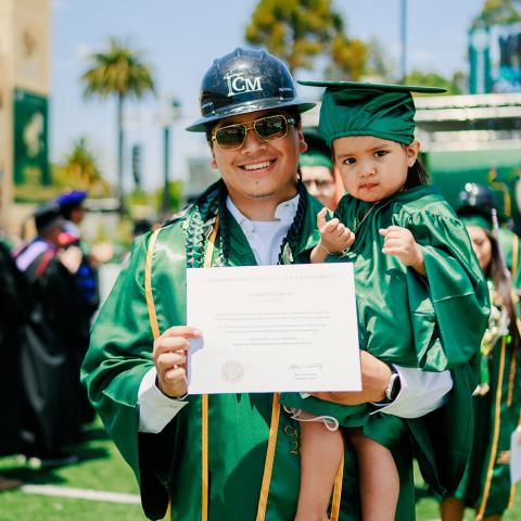 A graduate holds his child and shows his diploma during commencement ceremony.