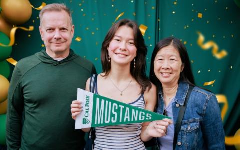 A student holds a Cal Poly pennant with her parents.
