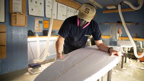 A person shaping a surfboard in the ASI Craft Center.