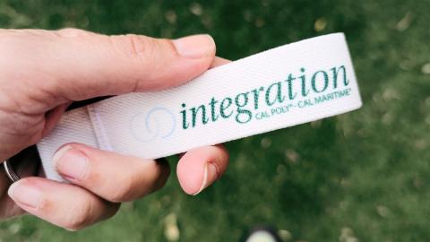 A person’s hand holding a wristband keychain with the Cal Poly-Cal Maritime integration logo on it.