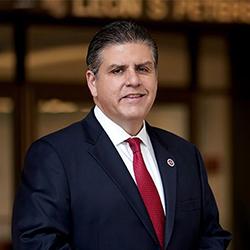 A headshot of Joseph Castro wearing a dark suit and red tie.
