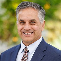 A headshot of Al Liddicoat wearing a navy-blue suit and red tie.