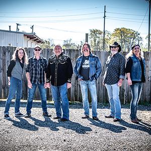 The Marshall Tucker Band lined up in front of a fence wearing blue jeans and dark T-shirts.