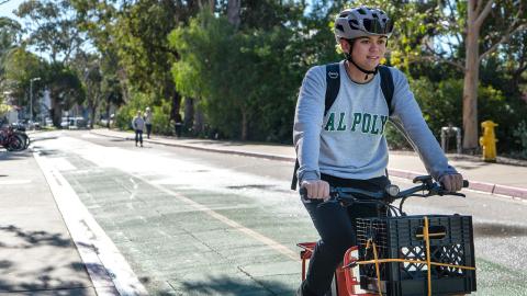 A person wearing a Cal Poly sweatshirt and bike helmet riding a bike on campus.