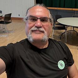 A headshot of Troy Weipert wearing a black shirt and glasses.