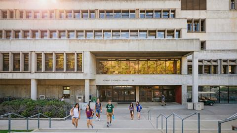 Students walking up the steps in front of the Robert E. Kennedy Library at dusk.