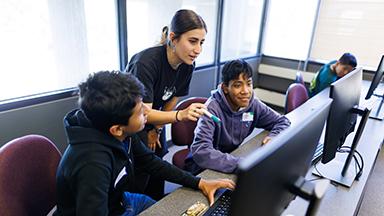 A college student helping two young boys on a computer.