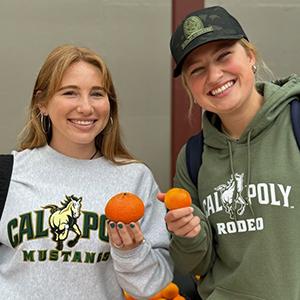 Two Cal Poly students holding tangerines and smiling at the camera.
