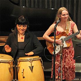 A woman playing hand drums and woman playing the guitar.