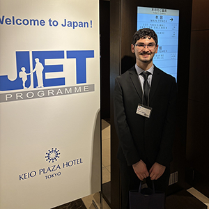 Enrique Lecha standing in front of a sign for the JET Program.
