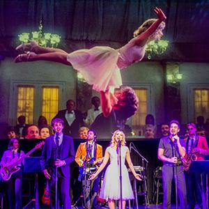 A scene from the movie “Dirty Dancing” playing on a screen behind performers on stage.