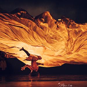A dancing spinning on stage beneath a flowing piece of fabric.