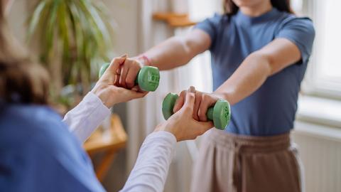 A student holding weights with assistance from a physical therapist.