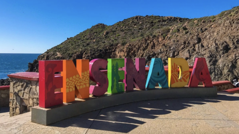 An image of multi-colored letters spelling out “Ensenada” with hills and the ocean in the background.